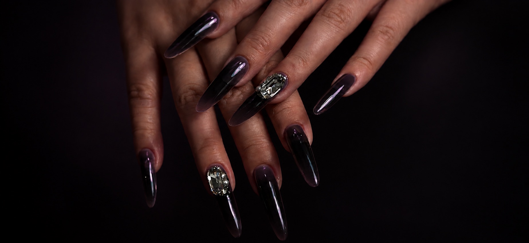 Hands with long translucent black nails, one set with a crystal